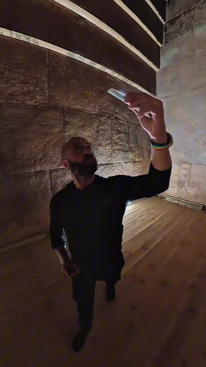 Michel inside the burial chamber, phone light raised to the corbelled ceiling
